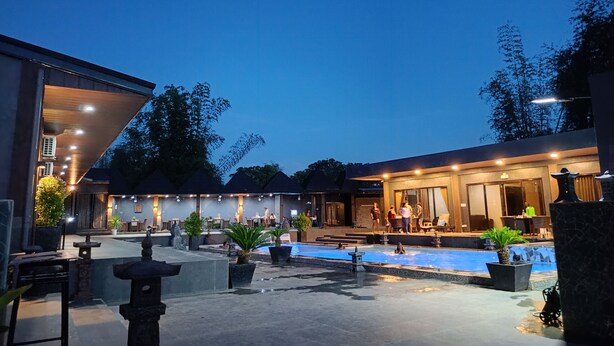 A pool area with a stone pathway, potted plants, and a building with a covered seating area. - DE PORCH (Bolinao)