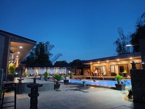 A pool area with a stone pathway, potted plants, and a building with a covered seating area. - DE PORCH (Bolinao)