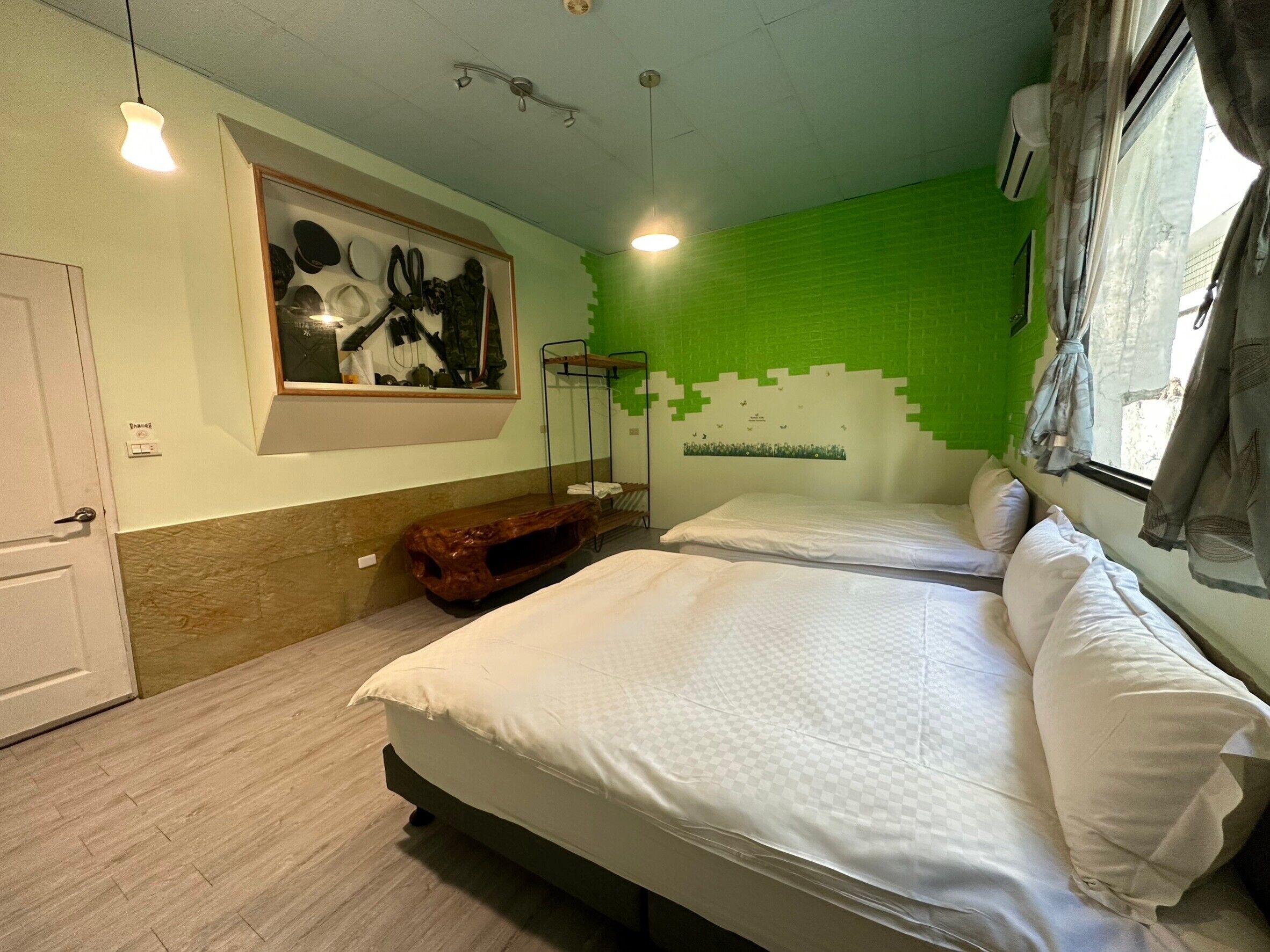A hotel room with two beds, a wooden bench, a wall-mounted shelf, and a green wall design.