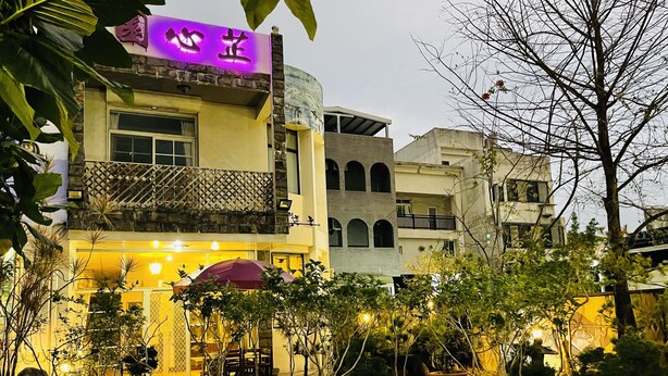 A building with a purple sign, outdoor seating, and potted plants. - Zhi Xin Yuan (Hualien City)