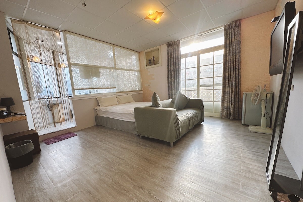 A spacious living area with a sofa, a bed, and a large window providing natural light.