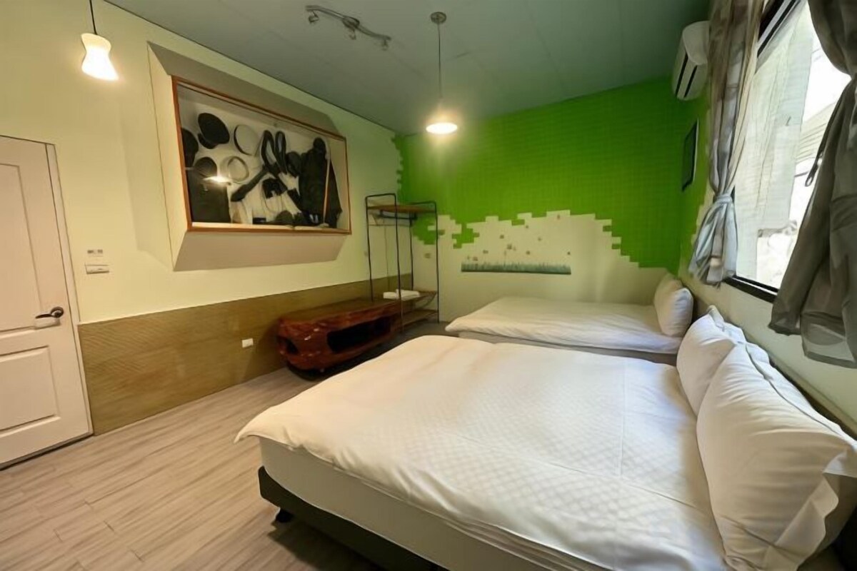 A hotel room with two beds, a bunk bed, a painting, and a green wall.