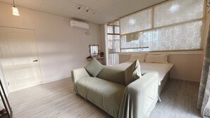 A room with a bed, a sofa, a window with lace curtains, a wall-mounted air conditioner, and a door. - Zhi Xin Yuan (Hualien City)