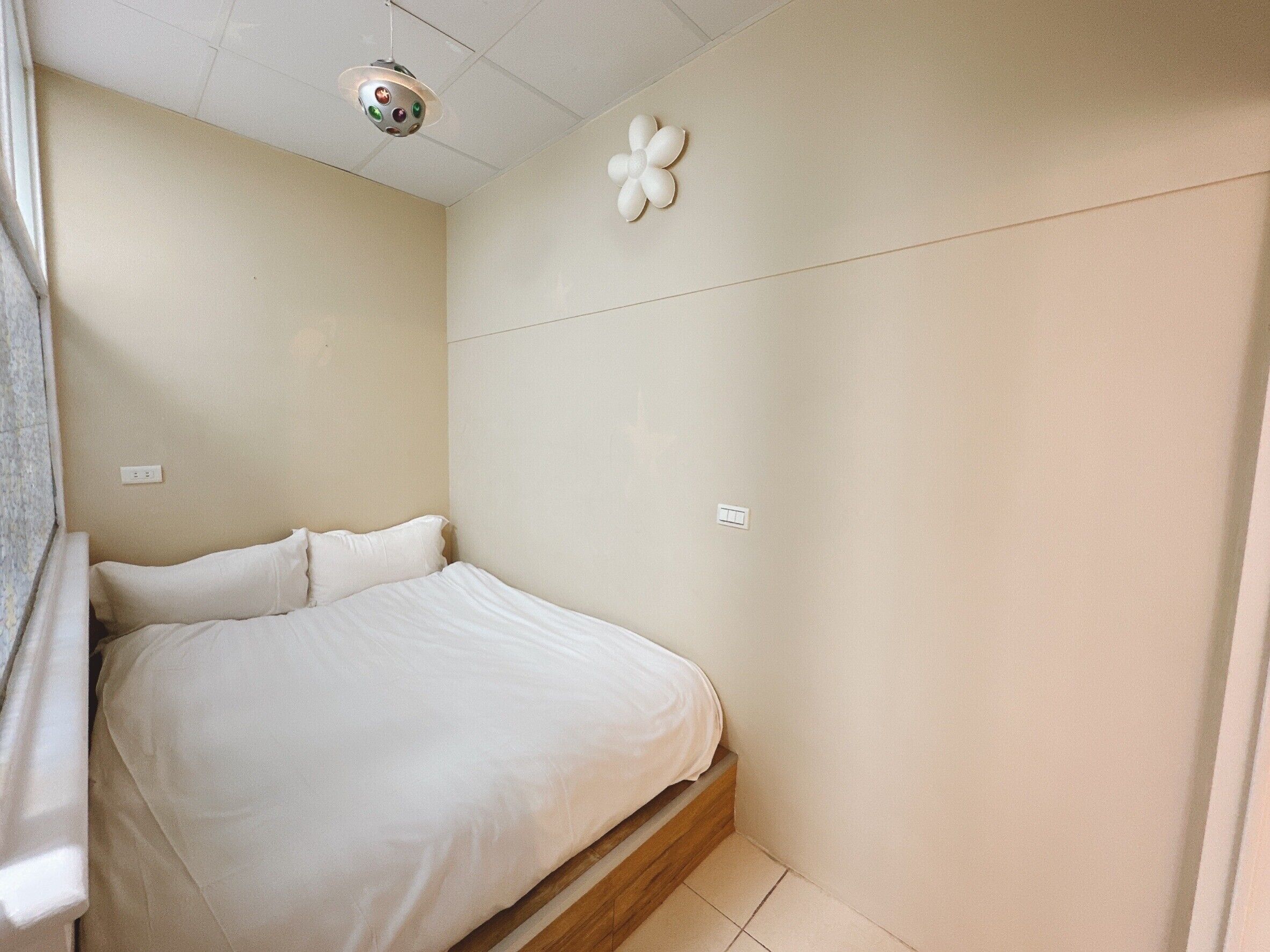 A small, neatly made bed in a room with a plain wall and a ceiling-mounted light fixture.