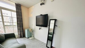 A room with a sofa, a standing fan, a TV mounted on the wall, and a mirror leaning against the wall. - Zhi Xin Yuan (Hualien City)