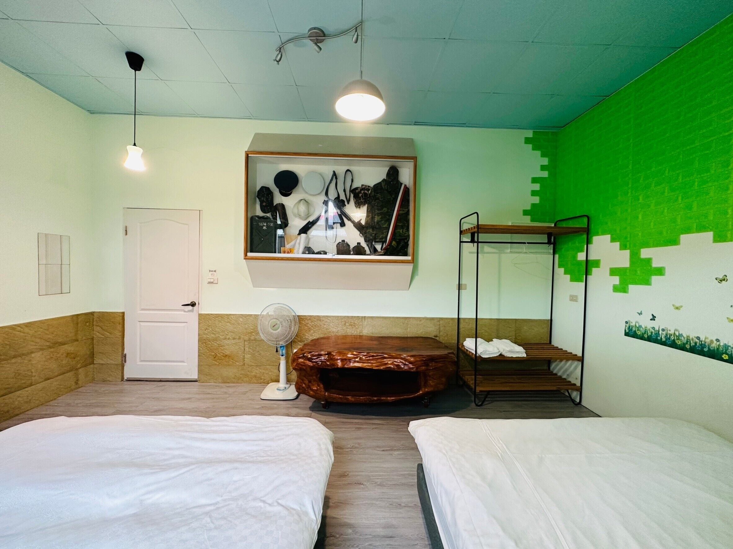 Une chambre avec deux lits, un ventilateur, une œuvre d’art encadrée et un mur décoré dans des tons verts.