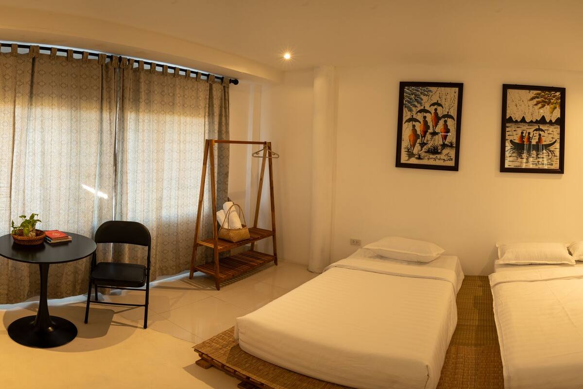 Habitación de hotel con dos camas, una mesita con sillas, un sillón colgante y dos cuadros en la pared.