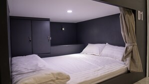 A single bed with white bedding, a dark wall, a ceiling light, and a door with a number sign. - Remedy Hostel (Vientiane)