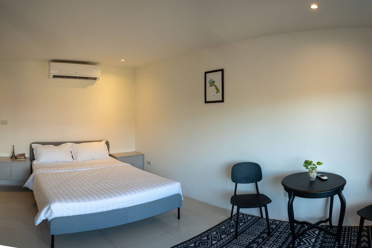 Un dormitorio moderno con cama, mesitas de noche, una pequeña mesa con sillas y un aire acondicionado instalado en la pared.