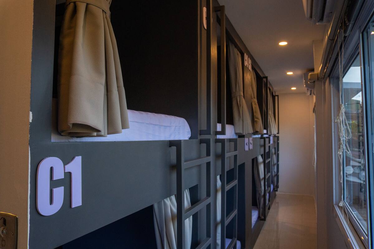 Habitación con literas, un cartel con el número 'C1', una ventana con cortinas y un pasillo con una puerta.