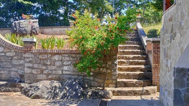 Eine Steintreppe führt zu einem Gebäude mit einer Steinmauer und einem kleinen Garten mit Pflanzen und einem Felsen.