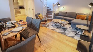 A modern living room with a sofa, dining table, and chairs. There is a staircase leading to an upper level. - Spring Rose (Bedale)