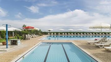 Relax by the two pools surrounded by lounge chairs and umbrellas, set amidst lush greenery and potted plants.