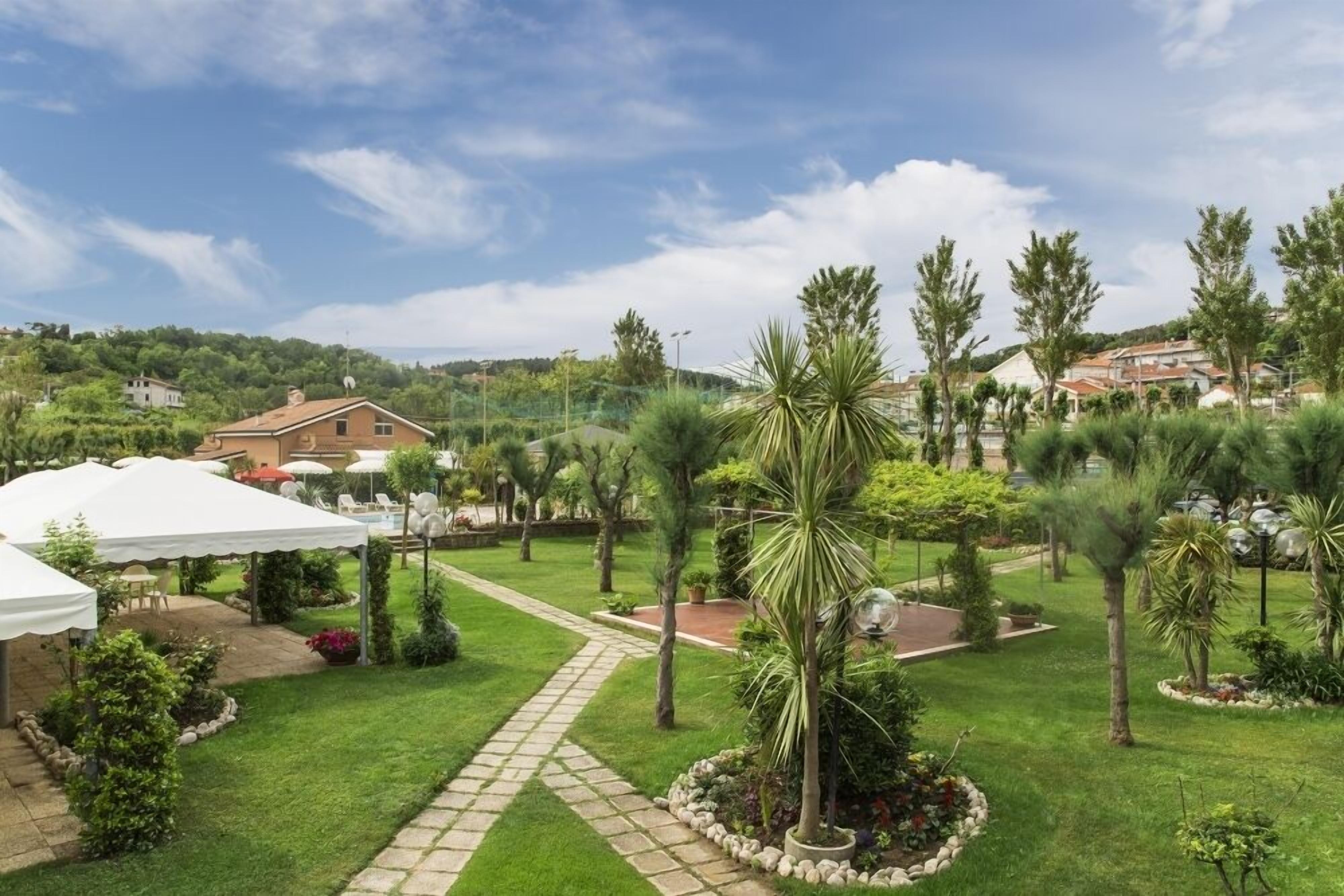 A well-maintained garden with a paved pathway, palm trees, and a white tent.
