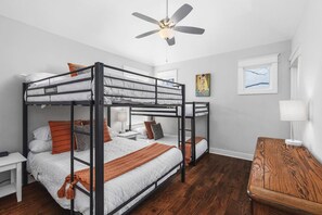 Habitación con literas, ventilador de techo, mesita de noche y una mesita auxiliar de madera.