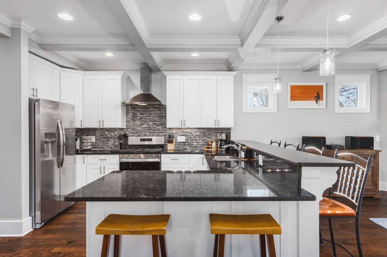 A modern kitchen with white cabinets, a large island, and a stainless steel refrigerator.