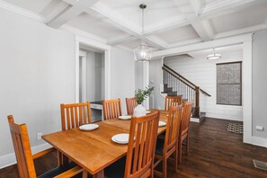 A dining room with a wooden table and chairs, a hanging light fixture, and a staircase leading to another room.