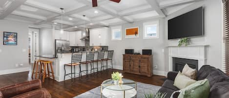 Un salón amplio con chimenea, ventilador de techo y una cocina al fondo.