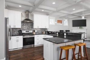 A modern kitchen with white cabinetry, a black countertop island, stainless steel appliances, and wooden stools.