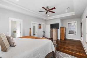 A spacious bedroom with a large bed, a ceiling fan, a wooden floor, and a view of the outside through a window.