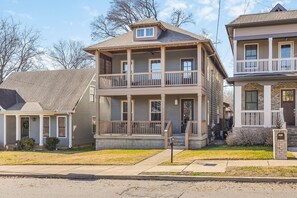 A two-story residential building with a balcony, a front porch, and a stone foundation.