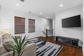 Una sala de estar moderna con un sofá, un televisor montado en la pared y una escalera que conduce a otro nivel.