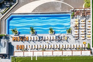 Une piscine sur le toit, avec un motif ondulatoire, entourée de chaises longues et de palmiers.