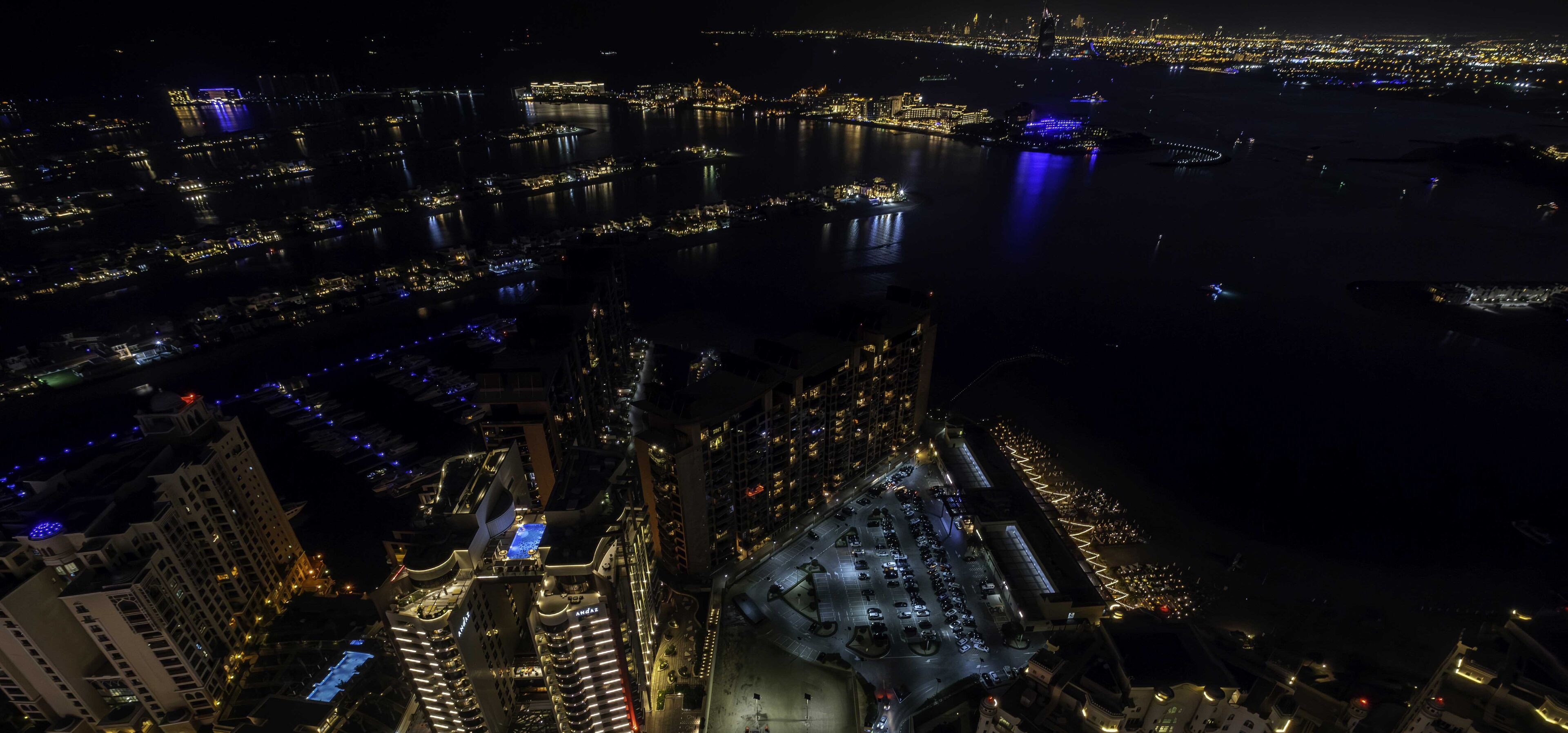 An aerial view of a cityscape at night with illuminated buildings, a river, and a parking area.