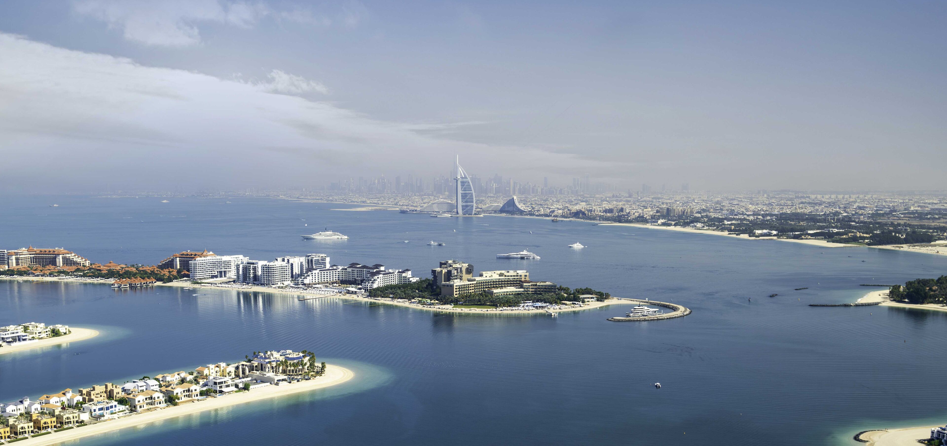 A coastal cityscape with a prominent modern tower, a marina with yachts, and a densely built urban area in the background.