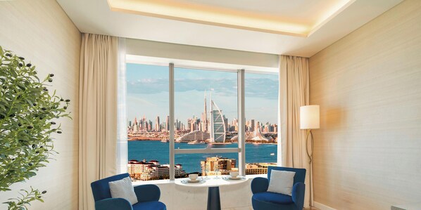 A room with a large window offering a cityscape view, a table with a cup and saucer, and two blue chairs.