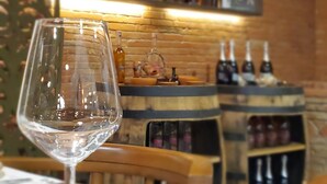 Ein Weinglas auf einem Tisch, eine Speisekarte, ein Holzstuhl und im Hintergrund eine Bar mit Regalen voller Weinflaschen.