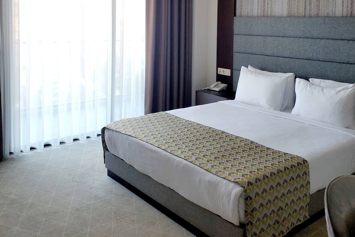 A hotel room with a large bed, a nightstand, a telephone, and a window with curtains.
