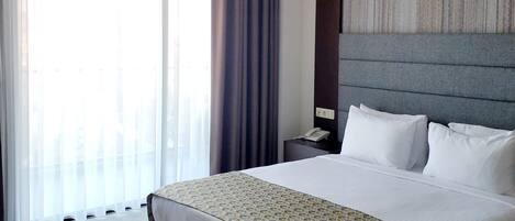 Quarto de hotel com uma cama grande, mesa de cabeceira, telefone e janela com cortinas.
