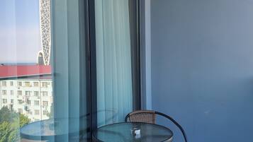 A balcony with a glass table and wicker chairs, overlooking a building with a distinctive tower.