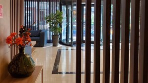 Eine moderne Hotelhalle mit einem Holzbuffet, einer Topfpflanze und Blick auf die Straße durch große Glasfenster.