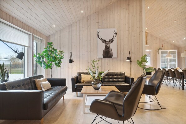 Ein modernes Interieur mit Holzbalkendecke, Ledersofas, einem Couchtisch und einem Essbereich mit Stühlen.