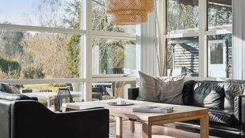 A modern living room with a large window, a wooden coffee table, a black leather sofa, and a wicker hanging light fixture.