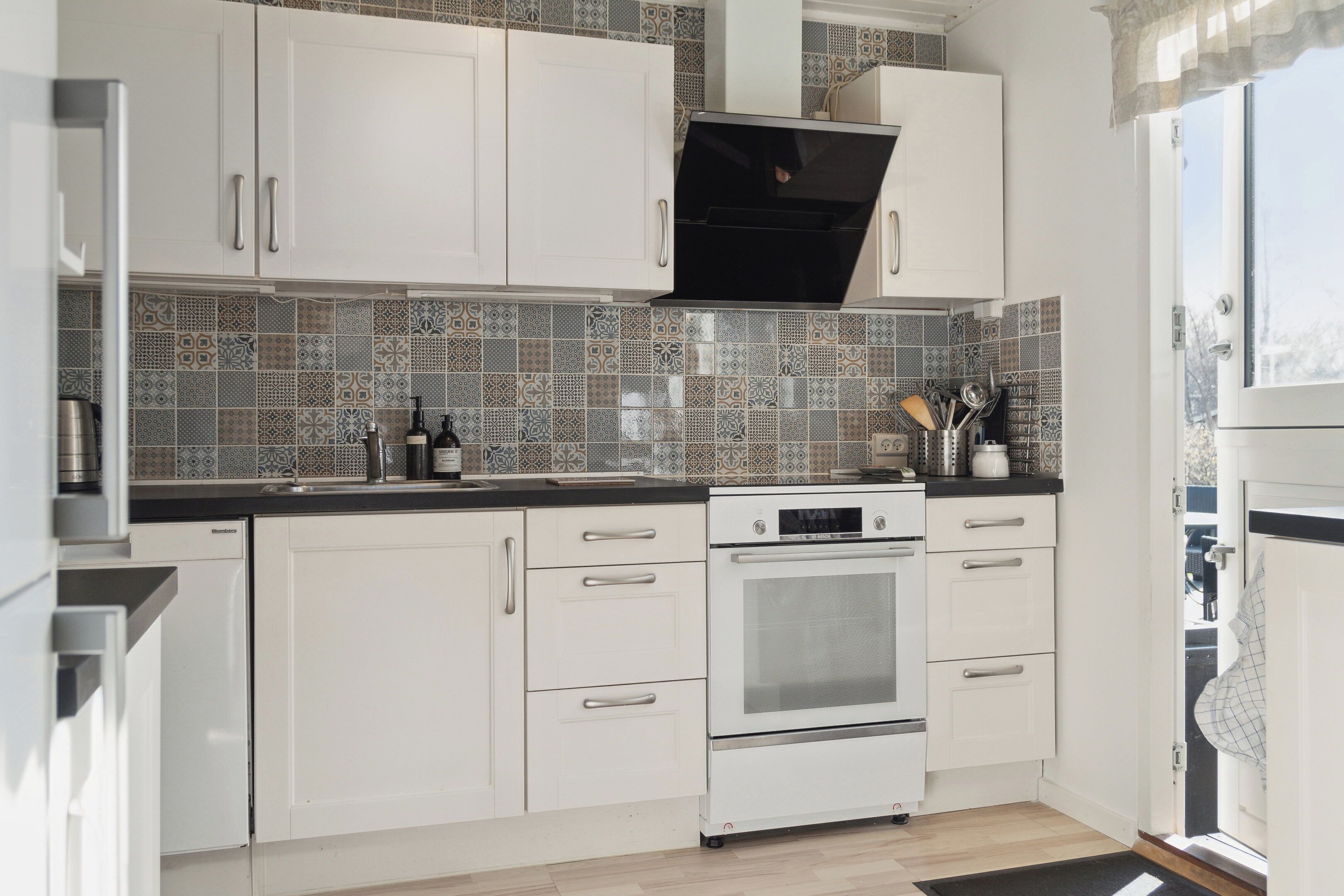 A kitchen with white cabinets, a black oven, and patterned backsplash tiles.