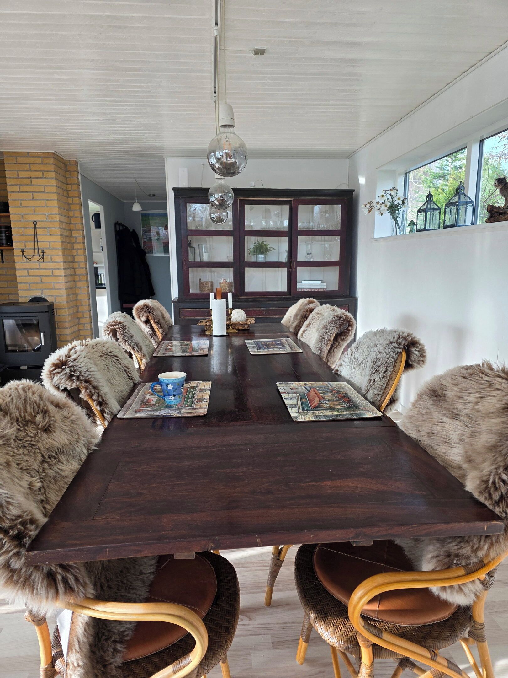 A dining room with a long table, chairs with fur throws, and a chandelier.