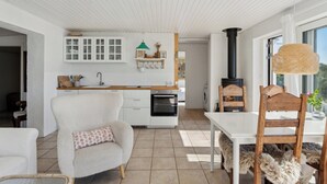 A modern kitchen with white cabinetry, a wooden dining table, and a large window. - Lovely beach house with panoramic view (Martofte)