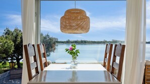 A table with chairs, a hanging light fixture, and a view of a lake through a window. - Lovely beach house with panoramic view (Martofte)