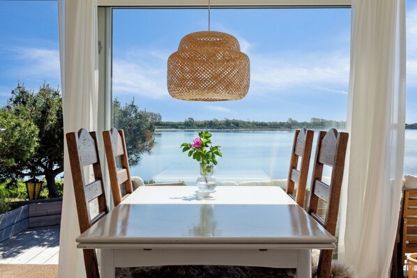 A table with chairs, a hanging light fixture, and a view of a lake through a window.