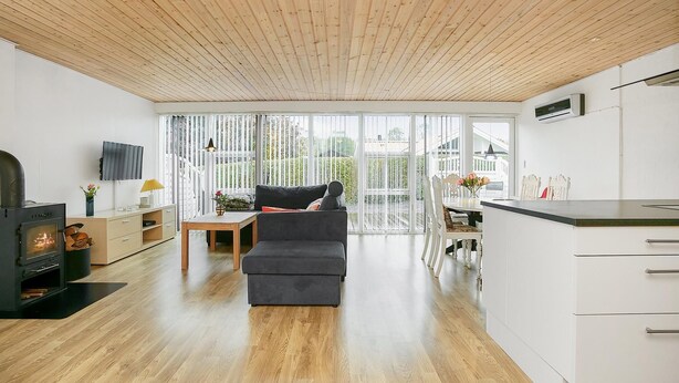 A modern living room with a sofa, a fireplace, and a kitchen area with cabinets and a countertop. - Renovated summer house incl. cleaning and linen (Juelsminde)