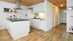 A modern kitchen with white cabinetry, a stainless steel range hood, and a wooden ceiling. - Renovated summer house incl. cleaning and linen (Juelsminde)