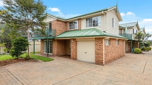 A two-story house with a garage, brick exterior, and a green roof. - Haw1.29 - Shells by Experience Jervis Bay (Huskisson)