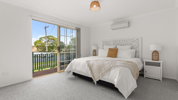 A bedroom with a large bed, a nightstand, a lamp, and a view of the outdoors. - Haw1.29 - Shells by Experience Jervis Bay (Huskisson)