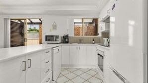 A modern kitchen with white cabinetry, a built-in microwave, a coffee maker, and a kettle. - Haw1.29 - Shells by Experience Jervis Bay (Huskisson)