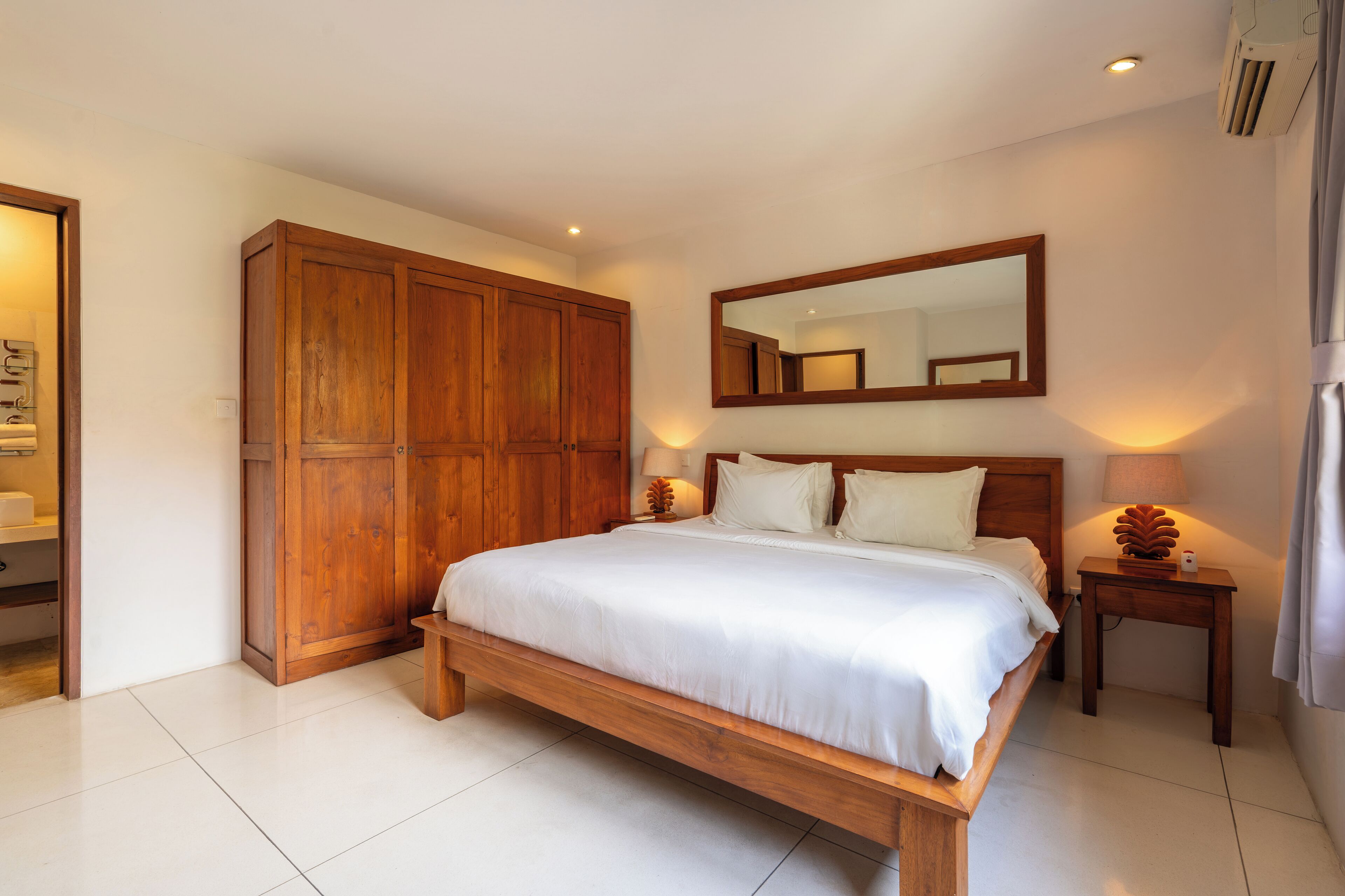 Un dormitorio con una cama de madera, un armario grande, una mesita de noche con una lámpara y un espejo en la pared.