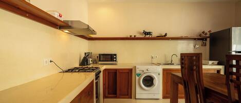 A compact kitchen with a microwave, stove, washing machine, and wooden cabinets.
