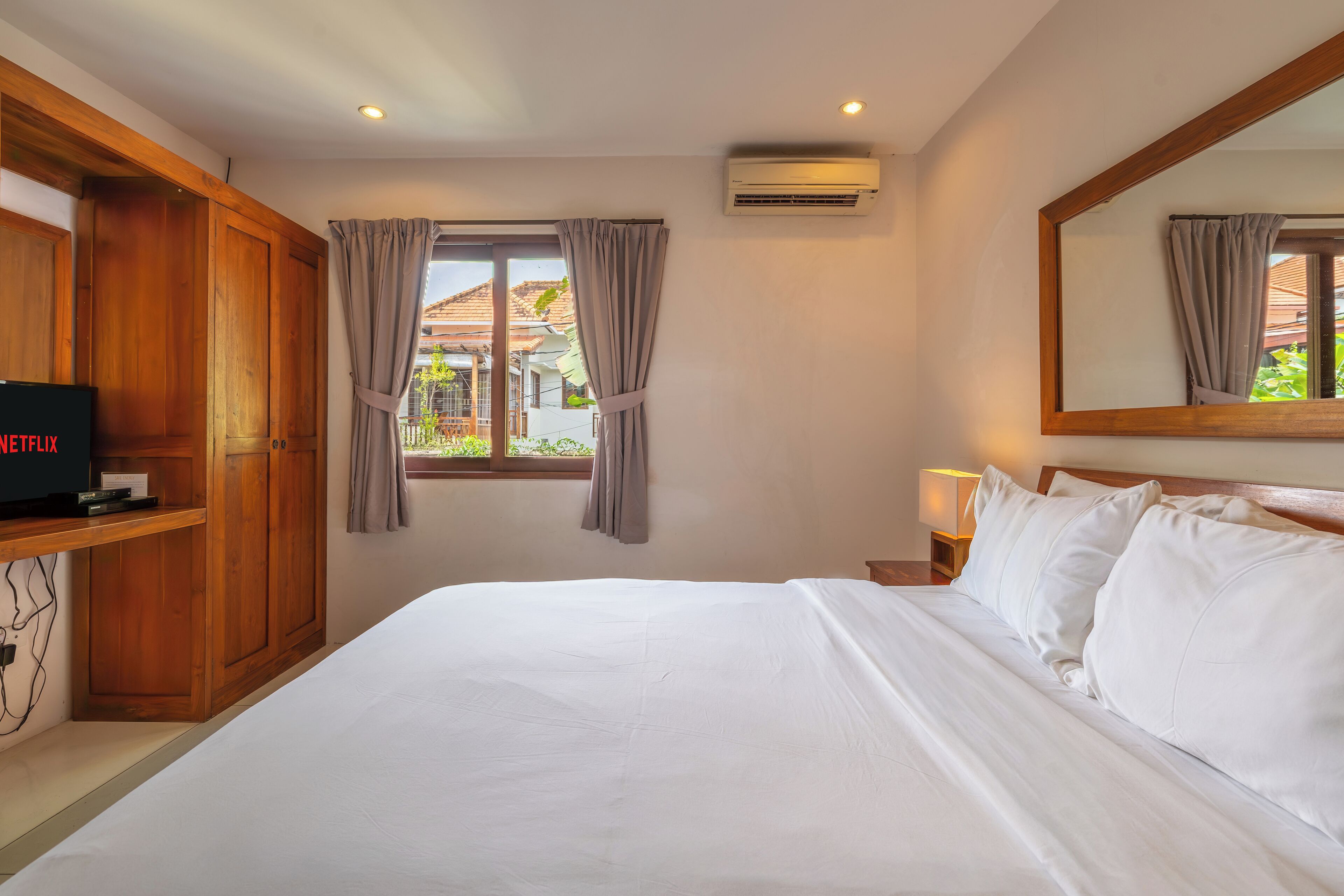Een hotelkamer met een groot bed, een houten garderobe, een televisie en een raam met gordijnen.